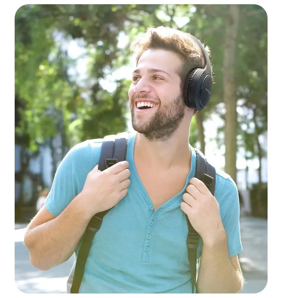 Homem sorrindo ao ar livre, usando fone de ouvido preto e mochila, aproveitando música.