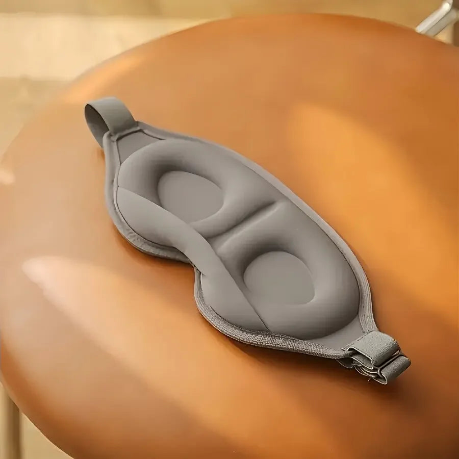 Máscara de dormir cinza anatômica sobre uma cadeira marrom, acessório para sono