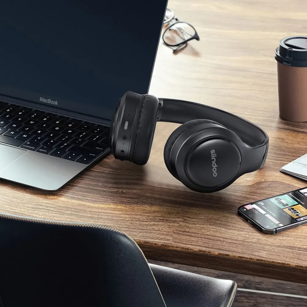 Fone de ouvido Bluetooth Sinodo preto sobre mesa com notebook MacBook e smartphone.