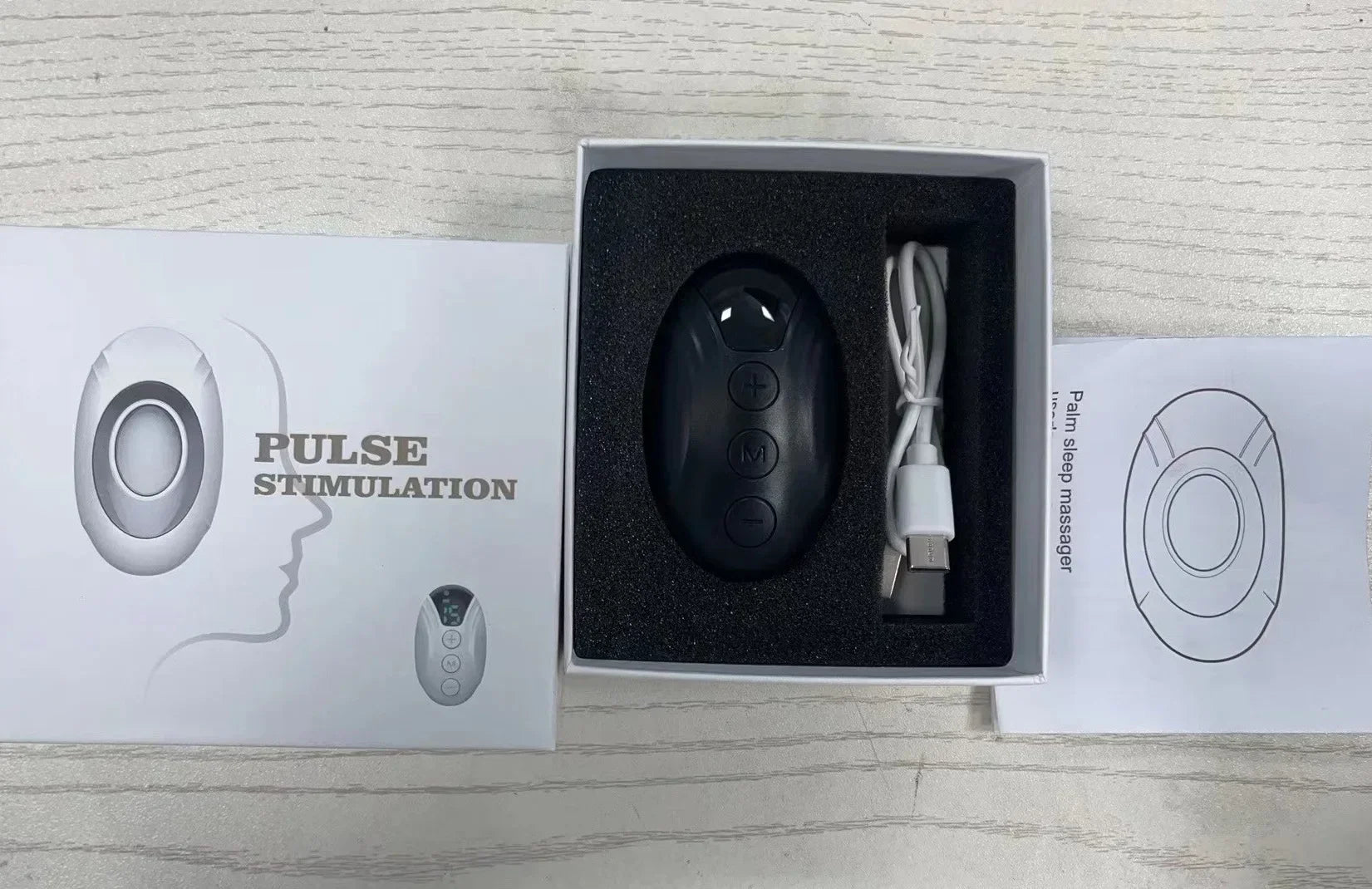 Massageador de pulso preto com cabo USB em caixa, embalagem pulse stimulation sobre mesa